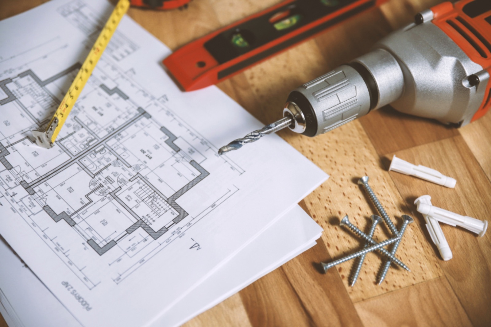 Floor plan drawing with a drill, level and screws on a workbench